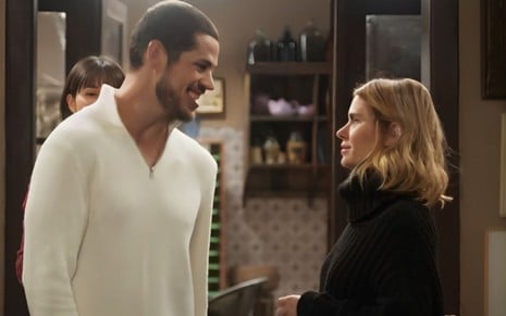 Em cena de Vai na Fé, José Loreto, de blusa branca, sorri ao conversar com Carolina Dieckmann, que usa roupa preta