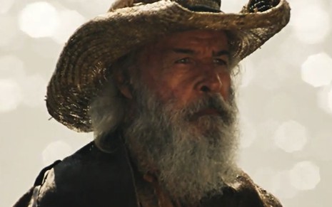 Osmar Prado usa barba longa, chapéu e um manto e está caracterizado como o Velho do Rio para a novela Pantanal