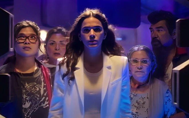 Bruna Marquezine sai de elevador com terninho branco e expressão séria em cena de Besouro Azul