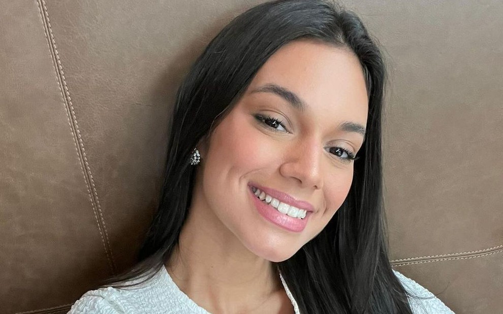 Alane Dias posa sorrindo usando uma blusa branca