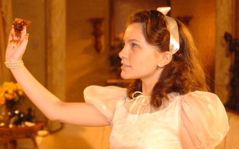 A atriz Cecilia Dassi com mão suja de chocolate, expressão séria, olhando para a esquerda em cena de Alma Gêmea