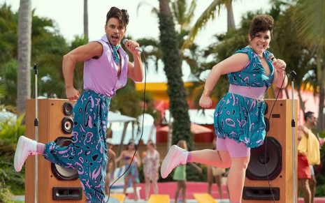 Com roupas chamativas, Rodrigo Urquidi e Rossana De Leon se apresentam em um palco à beira da piscina em cena de Acapulco
