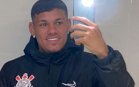O jogador Dimas de Oliveira com um moleton com escudo do Corinthians faz selfie com celular na mão