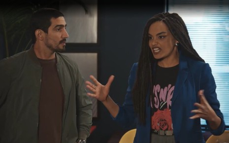 Os atores Renato Góes e Lucy Ramos lado a lado, ela com expressão de raiva, gesticulando com as mãos, em cena de Família É Tudo