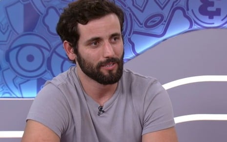 Matteus Amaral usa uma camiseta cinza e parece pensativo no Bate-Papo BBB