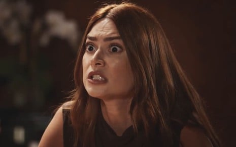 Thaila Ayala caracterizada como Elisa; ela está com os olhos arregalados e mostra os dentes, em agonia, durante cena de Família É Tudo