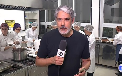 Com camiseta preta informal, William Bonner segura microfone com canopla da Globo no Jornal Nacional de 11 de maio de 2024