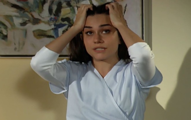 Alessandra Negrini caracterizada como Puala; ela usa a roupa de hospital e está com as mãos na cabeça, desesperada, em cena de Paraíso Tropical
