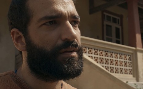 Humberto Carrão caracterizado como José Inocêncio; ele usa uma camisa laranja de lã e parece tenso em cena de Renascer