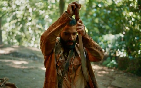 O ator Humberto Carrão está caracterizado como José Inocêncio em cena que ele finca um facão no chão no remake de Renascer