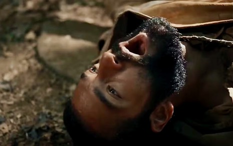 Humberto Carrão está deitado e com a boca aberta simulando dor na novela Renascer como o personagem José Inocêncio