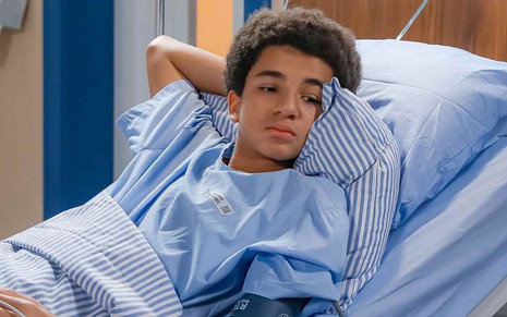O ator Miguel Schmid em cama de hospital, com expressão séria, em cena de A Infância de Romeu e Julieta