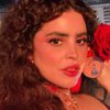 Natascha Falcão faz carão para foto; ela tem uma rosa vermelha no cabelo