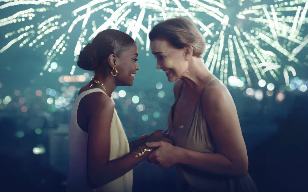 Jennifer Dias e Júlia Lemmertz em cena da série No Ano que Vem, de mãos dadas, em frente a paisagem noturna com fogos de artifício