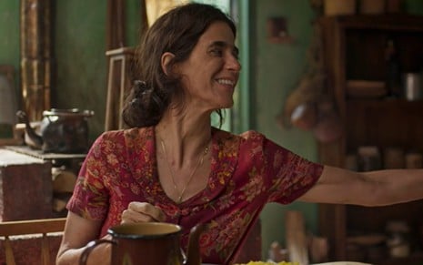 A atriz Mariana Lima sorrindo e esticando o braço para a direita em cena de No Rancho Fundo