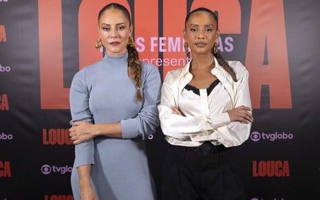 Paolla Oliveira usa vestido azul e está posando ao lado de Taís Araujo, que usa calça preta e blusa branca com detalhes pretos