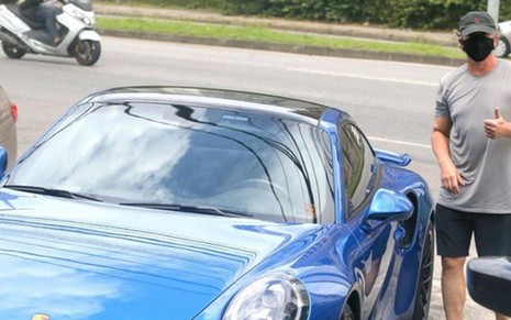 Reprodução de imagem de J. B. Oliveira ao lado de uma Porsche azul avaliada em mais de 1 milhão de reais