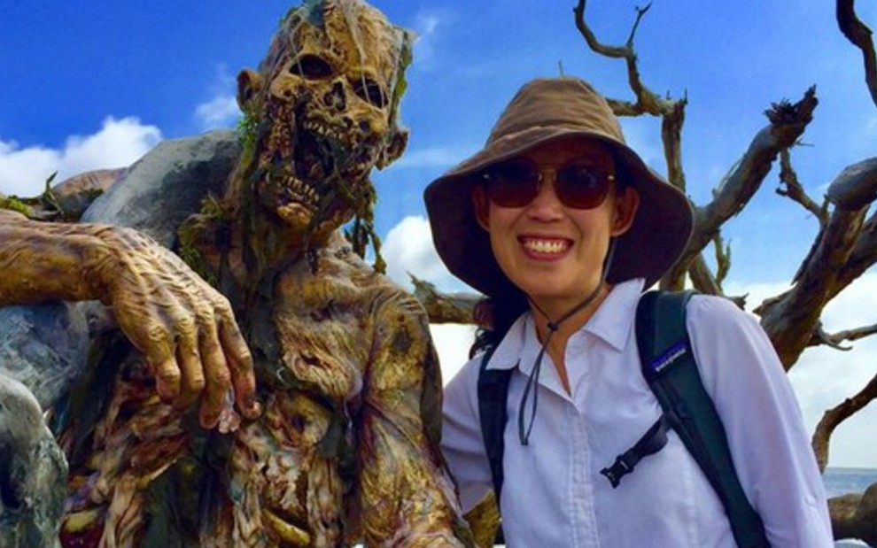 Um zumbi esqulético posa para foto ao lado da roteirista Angela Kang, que usa um chapéu e óculos escuro 