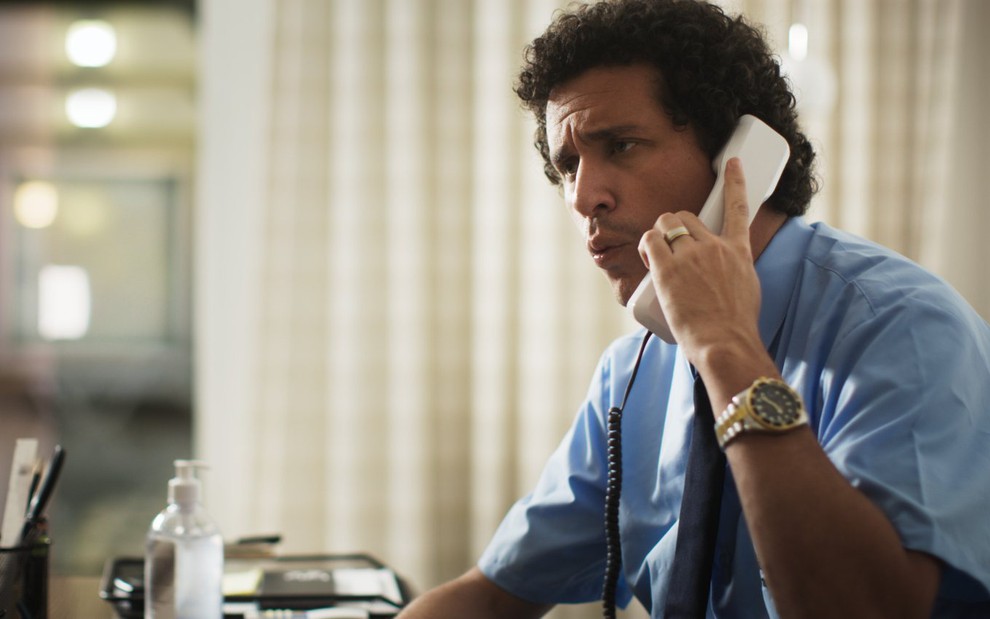 O ator Rafael Portugal fala ao telefone, de camisa e gravata, em cena da série 5X Comédia