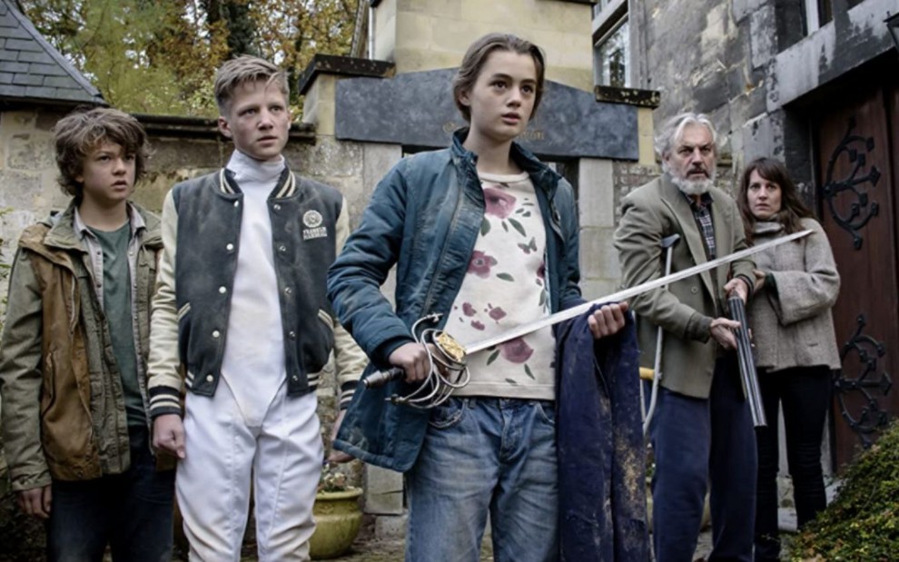 Nina Wyss segura uma espada na mão ao lado do elenco principal em foto do filme A Espada de D'Artagnan