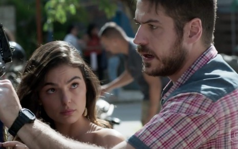 Os atores Isis Valverde e Marco Pigossi lado a lado, ela olha para ele, ele com expressão de irritação a ignora