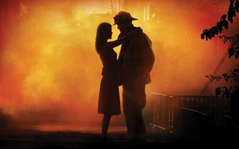 Uma mulher e um homem abraçados em meio a uma forte fumaça de cor alaranjada