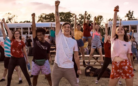 Um grupo de jovens com os braços direitos levantados em um cenário de acampamento no filme A Semana da Minha Vida