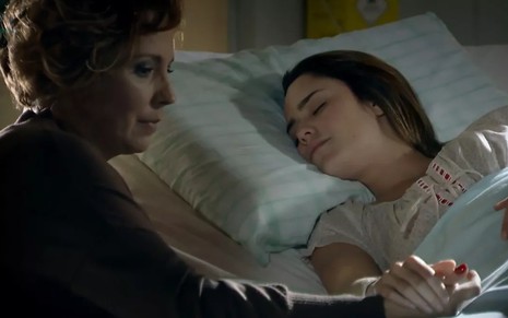 A atriz Ana Beatriz Nogueira ao lado de Fernanda Vasconcellos, em cena em cama de hospital; Fernanda dormindo e Ana Beatriz segurando a mão dela