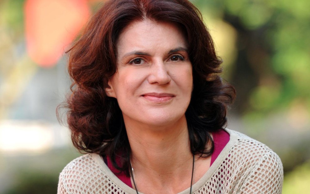 A autora Lícia Manzo com leve sorriso, de boca fechada, posa para foto em área externa