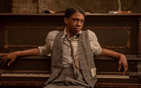 Chadwick Boseman sentado em frente a um piano em cena de A Voz Suprema do Blues