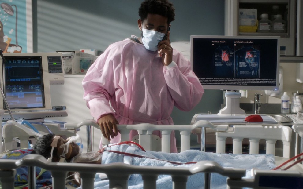 Daniel Augustin, com trajes de paciente hospitalar, observa um bebê intubado em cena de Grey's Anatomy