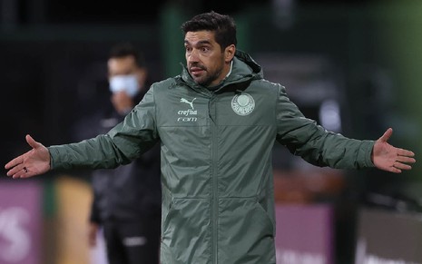 Abel Ferreira de jaqueta cinza com símbolo do Palmeiras no lado direito de braços abertos com olhar questionador