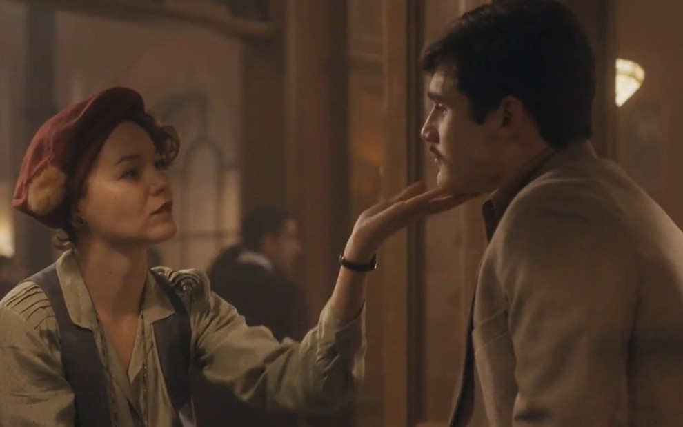 A atriz Joana de Verona encara Nicolas Prattes e coloca a mão no queixo dele. Ambos estão com roupas de época em cena como Adelaide e Alfredo em Éramos Seis