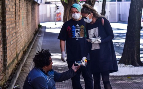 Imagem de Adriane Galisteu usando máscara e entregando marmita para morador de rua