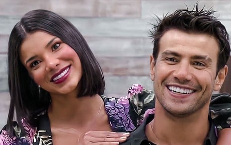 Jakelyne e Mariano está um do lado do outro; a modelo usa blusa florida e cabelo solto; ela sorri para frente da câmera; Mariano também sorri e usa camiseta preta