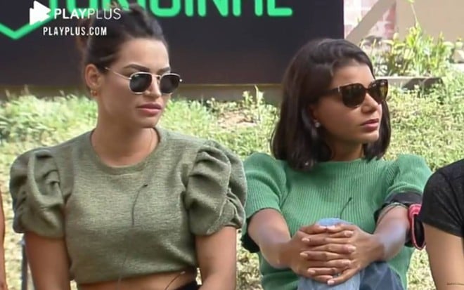 Raissa está usando uma blusa verde militar, óculos escuro; ao lado dela está Jakelyne, que também usa blusa verde e óculos escuro