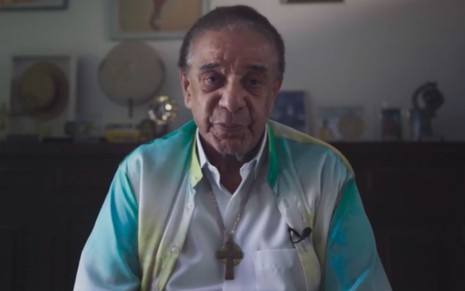 Agnaldo Timóteo usa camisa verde e branca com colar de cruz em sua casa em entrevista à série Doutor Castor, do Globoplay