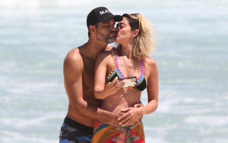 Bruno Cabrerizo e Carol Castro na Praia da Reserva nesta quinta (4): ator abraça atriz por trás, enquanto ela dá um beijo em seu rosto e segura um celular