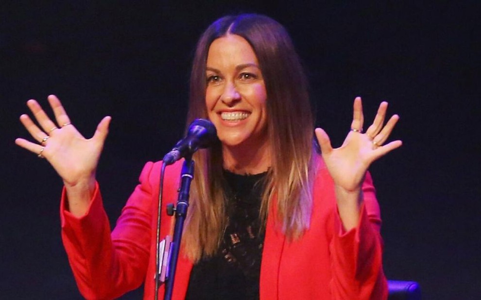 Imagem de Alanis Morissette com um casaco vermelho em cima do palco