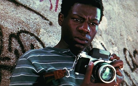 Buscapé (Alexandre Rodrigues) segura uma câmera fotográfica nas mãos em cena do filme Cidade de Deus (2002)