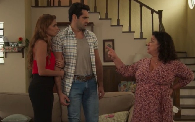 Em pé, a atriz Deborah Secco (Alexia/Josimara) e o ator João Baldasserini (Zezinho) olham assustados para a atriz Grace Gianoukas (Ermelinda), que aponta para o casal, em cena de Salve-se Quem Puder