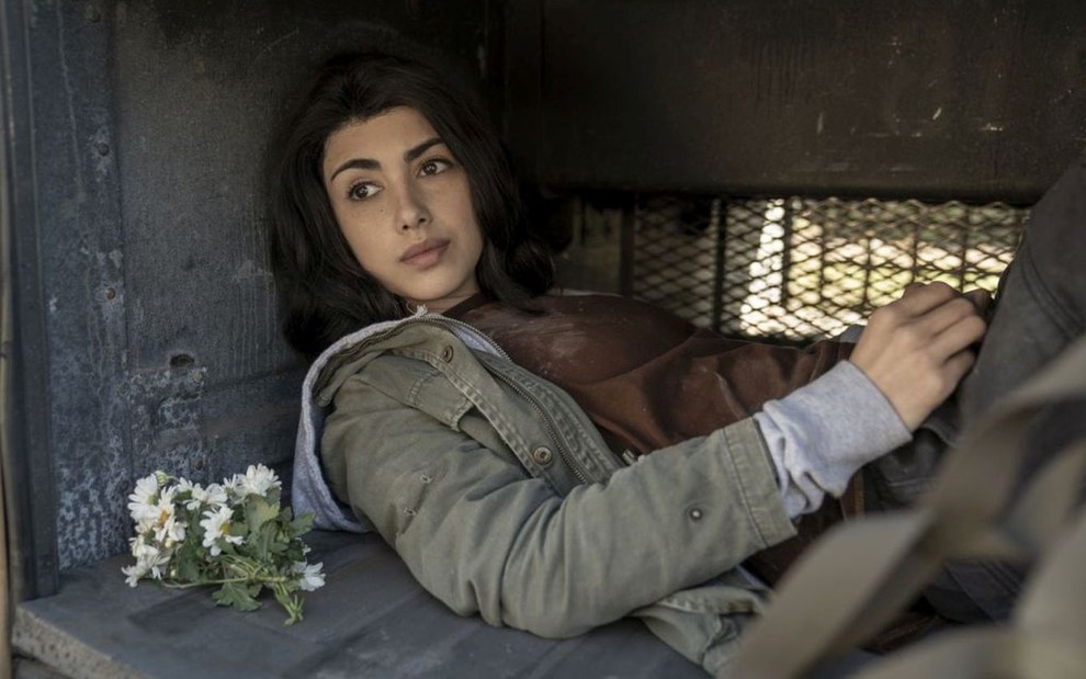 Alexa Mansour, caracterizada como Hope, está deitada no compartimento de bagagem de um ônibus em cena de Walking Dead: World Beyond