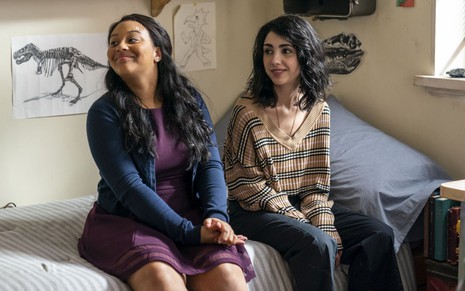 Sentadas em uma cama, as atrizes Aliyah Royale e Alexa Mansour têm expressões de curiosidade em cena de The Walking Dead: World Beyond