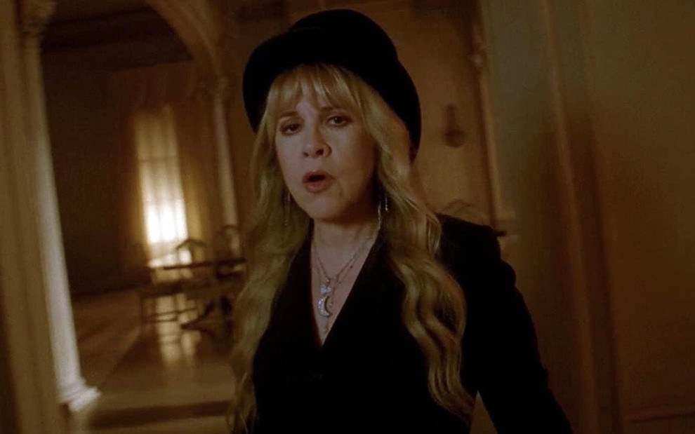 A cantora Stevie Nicks vestida de preto em uma sala de uma mansão vitoriana como a 'bruxa branca' da série American Horror Story: Coven