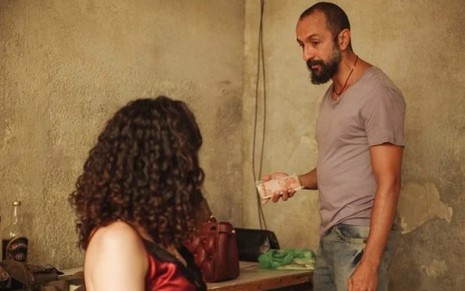 O ator Irandhir Santos com expressão séria, de frente para a atriz Clarissa Pinheiro, em cenário de cativeiro em Amor de Mãe