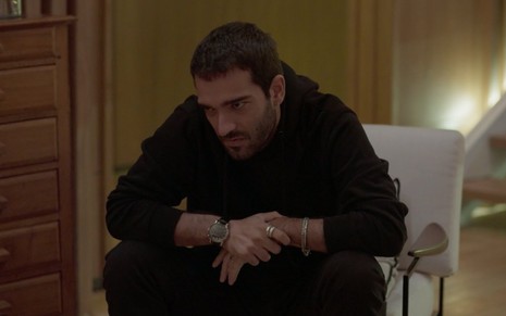 O ator Humberto Carrão cabisbaixo, de roupas pretas, em cena como Sandro em Amor de Mãe