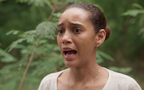 A atriz Taís Araujo com boca aberta e expressão de sofrimento em cena de Amor de Mãe em área externa e arborizada