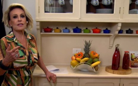 Ana Maria Braga de vestido colorido mostrando a cozinha de sua casa ainda desconhecida do público