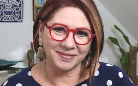 A psicóloga Anahy D'Amico, de óculos vermelhos, olha para a câmera em foto tirada em sua casa