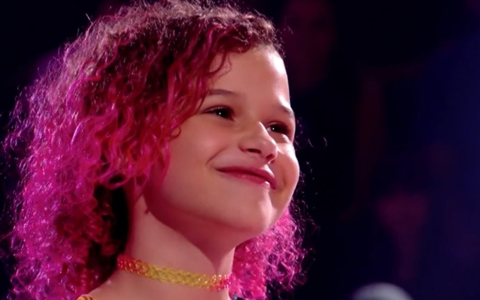 Analu Sampaio, de cabelos curtos e rosas, sorri após vencer a batalha do The Voice Kids